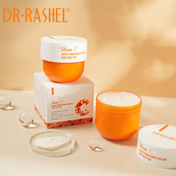Dr. Rashel Vitamin C Face & Body Scrub packaging and a small container with a clear lid, displayed on a table with decorative orbs and a soft focus background.